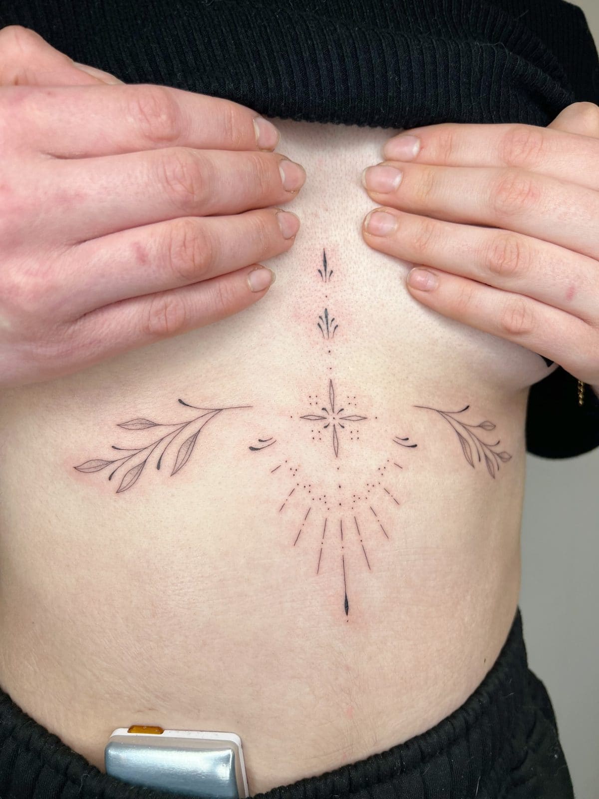 Ornement fine line et dot work sous la poitrine, avec deux branches de feuillage